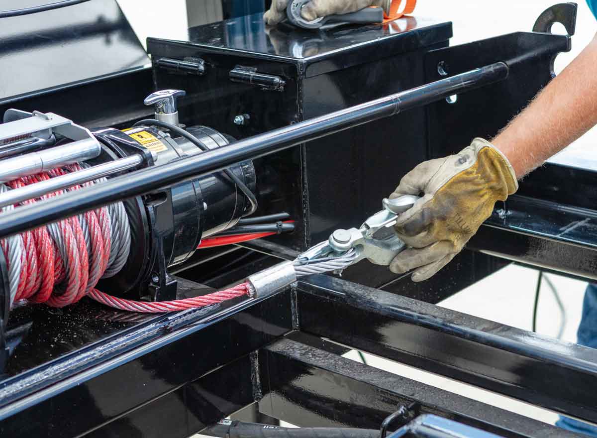 man wearing gloves is working on a trailer winch