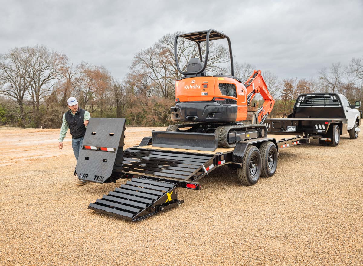 man is loading orange kubota excavator on a trailer with self stabilizing ramps